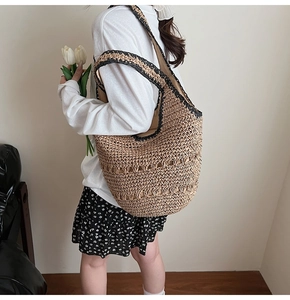 Detail of hand-woven straw bag featuring black contrast straps and intricate hollow pattern