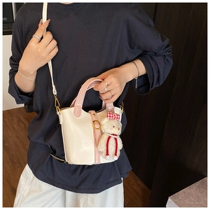 Detail of a white bucket bag with pink handles, gold buckle, and teddy bear charm