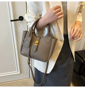 Detail of grey lychee leather bucket bag featuring gold buckle and cute puppy charm