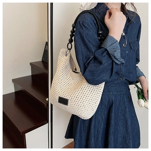 Detail of beige crochet bucket bag featuring black bead strap and dark leather logo label