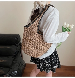 Detail of a woven straw shoulder bag featuring black trim accents and hollow-out patterns