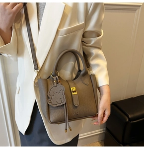 Detail of taupe lychee leather bucket bag with gold clasp and cute dog charm pendant
