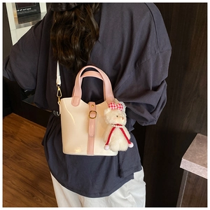 Dettaglio di una borsa a secchiello bianco crema con manici rosa e ciondolo a orsetto