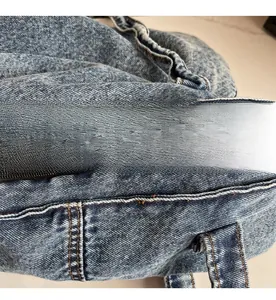 Detail of smooth gold metal zipper and orange stitching on light blue denim tote bag