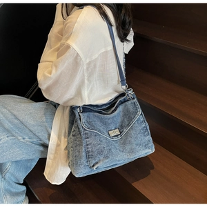 Détail du sac cabas en jean bleu avec bandoulière chaîne et fermoir pivotant en métal