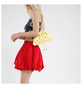 Detail of yellow bucket bag featuring silver rivets and drawstring closure worn by model