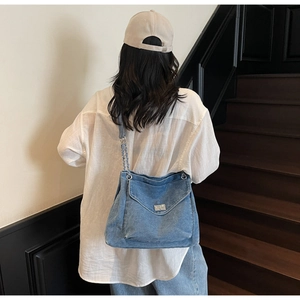Détails de la bandoulière en chaîne argentée et texture denim sur le grand sac cabas