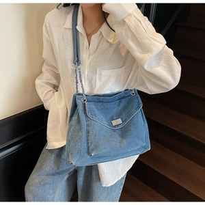 Detail of blue denim hobo bag with silver chain strap and metal twist lock on a shoulder