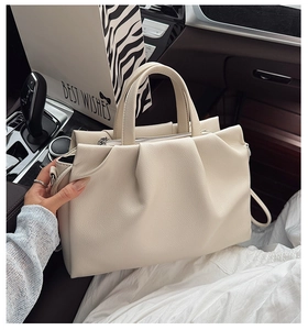 Detail view of the beige pleated handbag texture and handle in a car interior setting