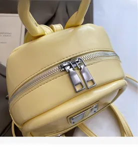 Detail of dual silver zippers on yellow PU leather mini backpack with metal logo plate