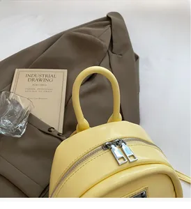 Detail of a bright yellow leather mini backpack with silver double zippers and handle