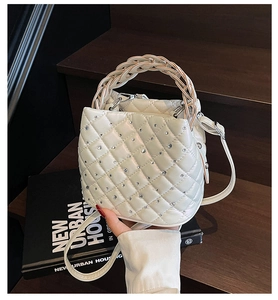 Detail view of white quilted bucket bag featuring rhinestone accents and woven handle