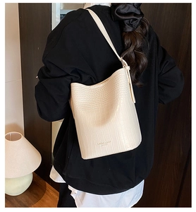Close-up of cream crocodile pattern bucket bag on model in cozy home setting