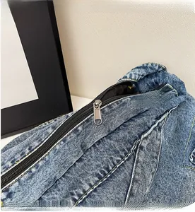 Detail of smooth metal zipper and yellow stitching on blue denim hobo bag