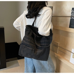 Detail of black washed denim tote bag featuring vintage jean pocket design and orange stitching