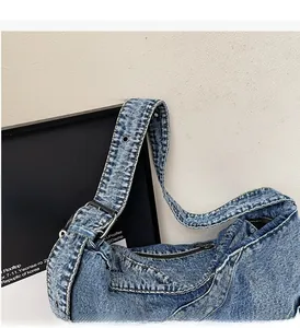 Detail of light blue denim shoulder bag featuring wide strap with silver metal eyelets