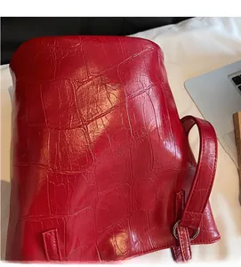 Close-up of red crocodile embossed leather tote bag showing metallic ring and brand logo