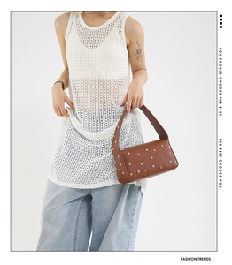 Detail of a brown leather shoulder bag featuring silver metal rivets and wide strap design