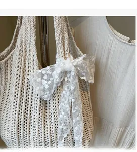 Detail of beige crochet handbag featuring intricate hollow knit and white floral lace bow