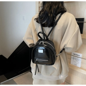 Detail of a shiny black mini backpack with silver metal plaque and adjustable straps