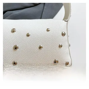 Detailed macro view of white pebble leather bag featuring decorative silver round studs