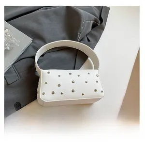 White baguette bag with silver rivets and lychee grain leather next to a phone for scale