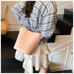 Detail of pink crocodile embossed leather bucket bag worn as a stylish crossbody purse