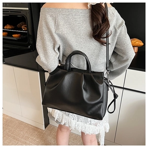 Detail of black large tote bag with lychee grain texture and pleated edges held by a model