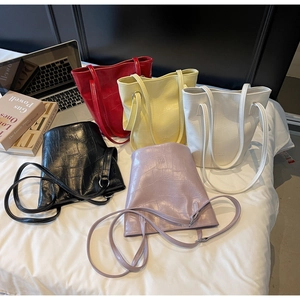 Detailed group shot of crocodile-patterned bucket bags in five colors on a white bed