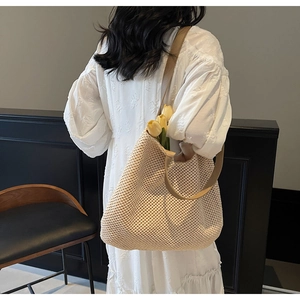 Detail of a large beige woven tote bag featuring a textured pattern and a brown shoulder strap