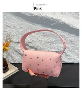 Pink litchi leather bag with silver rivets displayed against a stone wall