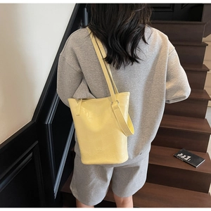 Detail showing lemon yellow crocodile embossed bucket bag with brand logo on shoulder