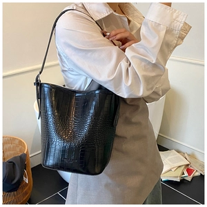 Detail of black crocodile pattern bucket bag with adjustable strap and embossed text