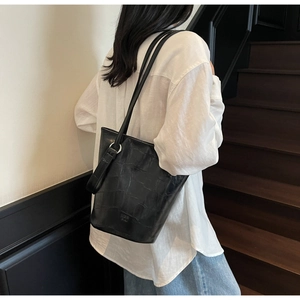 Detail showing the black crocodile embossed leather texture and silver metal ring of the bucket bag