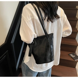 Detail of a black faux crocodile leather bucket bag shown on a model in a lifestyle setting