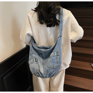 Detail of light blue denim crossbody bag with dual front utility pockets and wide strap
