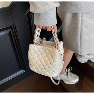 Close-up of beige quilted handbag featuring sparkling diamond studs and woven handle