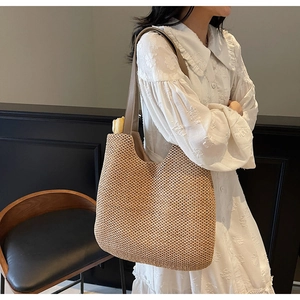 Detail view of woven straw tote bag with brown leather handles on shoulder
