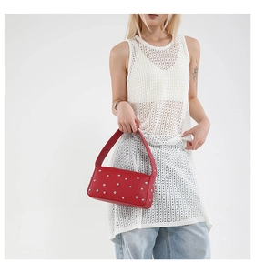 Detail of red leather underarm bag with silver rivets worn by a model in casual outfit