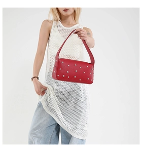 Detailed view of red pebble leather handbag with silver punk metal rivets on a model