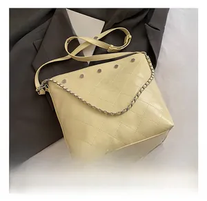 Detail of light yellow quilted bucket bag featuring silver buckle and chain strap