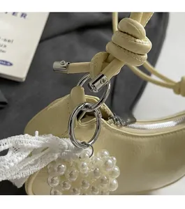 Detail of cream leather handbag with knotted strap, pearl cluster charm and lace ribbon