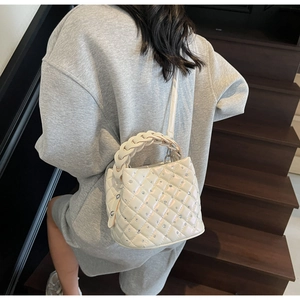 Detail of white quilted bucket bag with diamond studs and woven handle shown from the back
