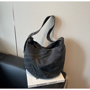Detail of dark denim crossbody bag featuring contrast stitching and adjustable metal buckle