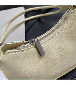Close-up of silver zipper hardware and pleated leather texture on beige shoulder bag
