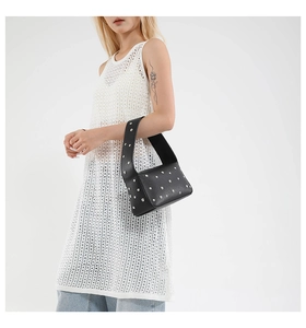 Close-up of black leather shoulder bag with silver studs worn by a model in casual outfit