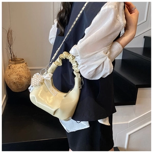 Détail du sac beige froncé avec un pendentif perle en cœur et un nœud en dentelle