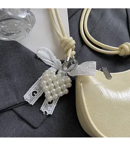 Detail of white pearl heart charm with lace bow on a light yellow leather bag