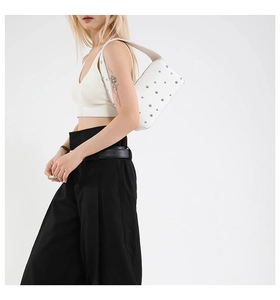 Detail of white underarm bag with silver studs worn by a model against a white wall
