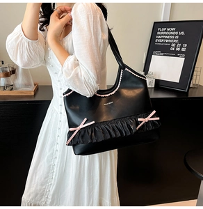Detail of black tote bag featuring pink bow accents and pleated skirt hem decoration
